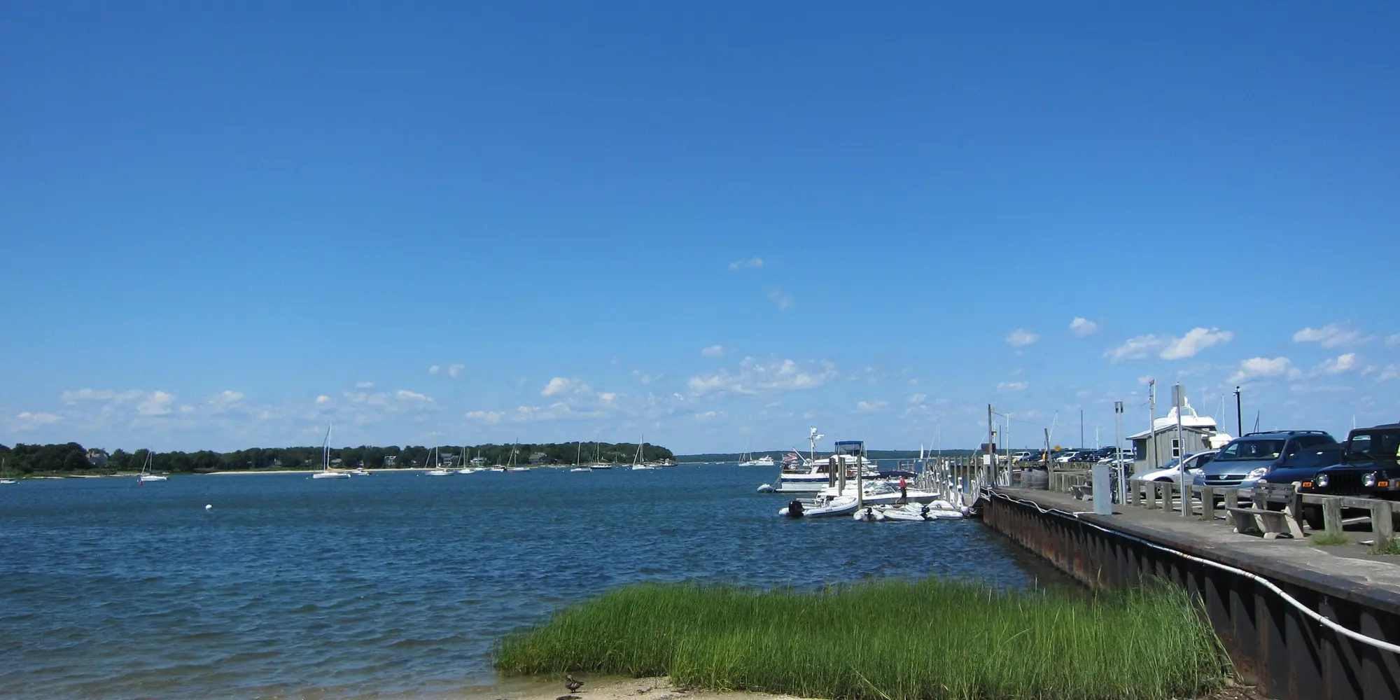 Sag Harbor Bay and the Long Wharf under a blue sky, with moored boats and a pier