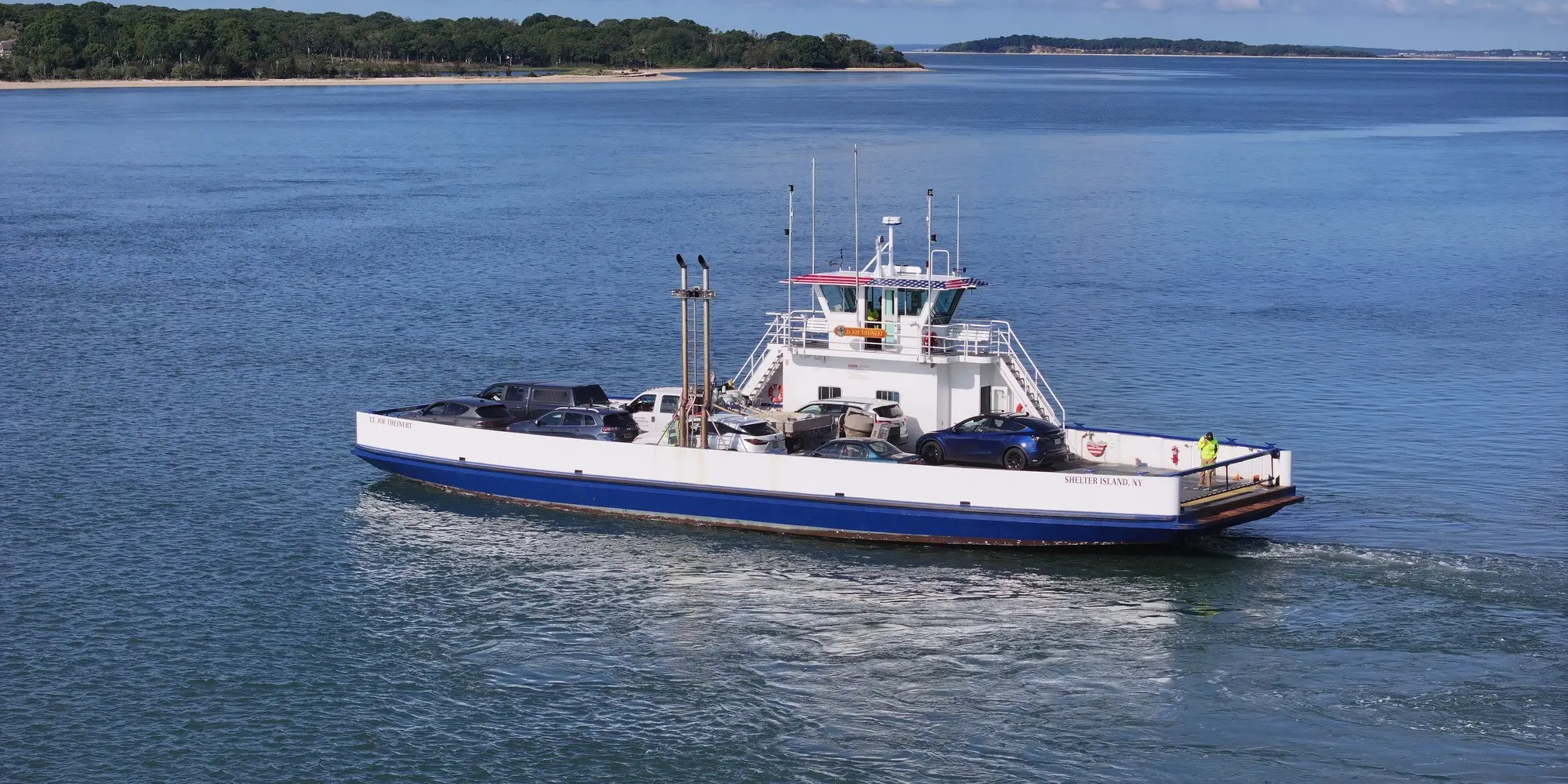 The Shelter Island South Ferry crossing blue water with a wooded shoreline behind